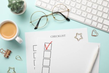 İşaretli onay kutusu, kahve, klavye, bardaklar ve ataçlar açık mavi arka planda düz konum