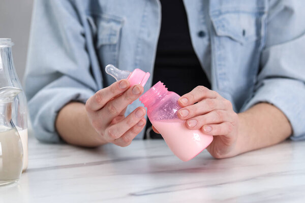 Mother making baby formula in feeding bottle at table indoors, closeup