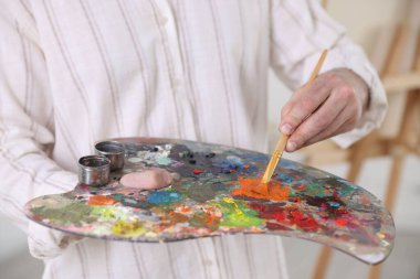 Sanatçının stüdyosunda boyaları palette karıştıran adam, yakın plan.