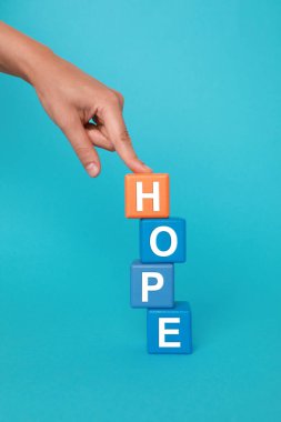 Açık mavi arkaplanda renkli küpleri olan Hope 'u seslendiren kadın.