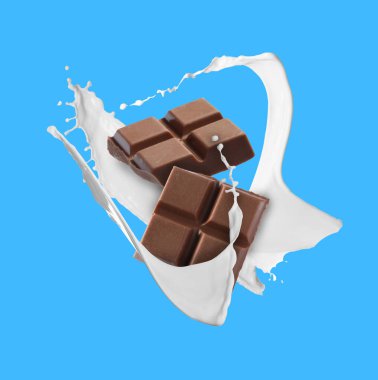 Nefis çikolata parçaları ve açık mavi arka planda havada sütün damlaları.