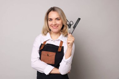 Taraklı ve makasla gri arka planda gülümseyen kuaför.