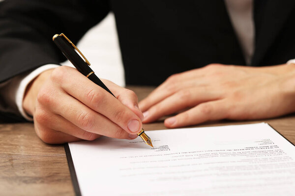 Человек подписывает лицензионный документ за деревянным столом в помещении, крупным планом