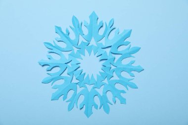 Açık mavi arkaplanda bir kağıt kar tanesi, üst manzara