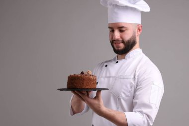 Üniformalı mutlu pastacı açık gri arka planda lezzetli çikolatalı pasta tutuyor.