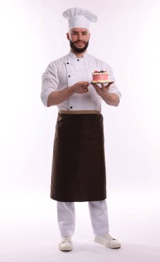 Üniformalı mutlu pastacı elinde beyaz arka planda böğürtlenli kek tutuyor.
