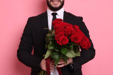 Pembe arka planda kırmızı gül buketi olan adam, yakın plan.