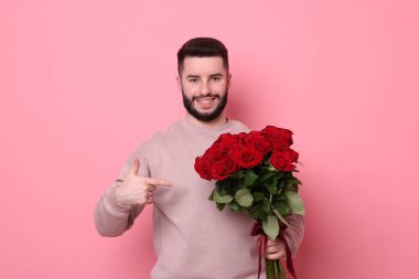 Pembe arka planda kırmızı güller açan mutlu bir adam.