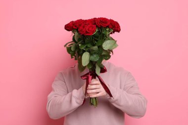 Pembe arka planda kırmızı gül buketi olan adam.