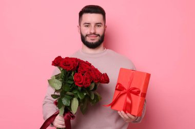 Kırmızı gül buketi ve pembe arka planda hediye kutusu olan bir adam.