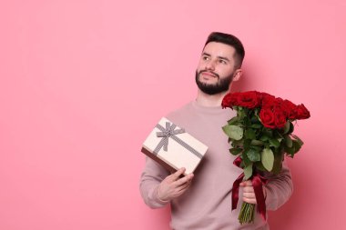 Kırmızı gül buketi ve pembe arka planda hediye kutusu olan bir adam.
