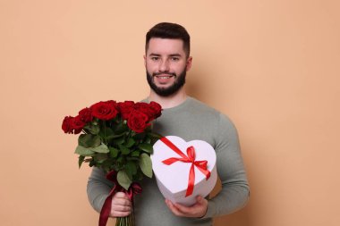 Kırmızı gül buketi ve bej arka planda hediye kutusu olan mutlu bir adam.