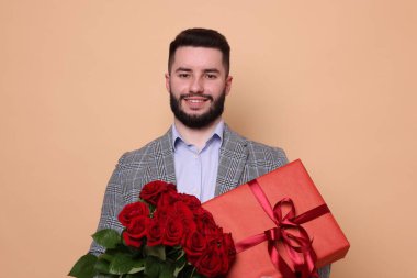 Kırmızı gül buketi ve bej arka planda hediye kutusu olan mutlu bir adam.