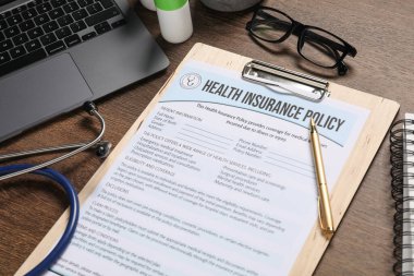 Sağlık sigortası formu, dizüstü bilgisayar, steteskop, gözlük ve kalem tahtada, yakın plan.