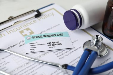 Sağlık sigortası kartı, poliçe, steteskop ve şişeler beyaz masada, yakın plan.