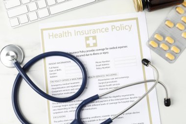 Sağlık sigortası poliçesi, steteskop ve beyaz mermer masa üzerindeki haplar.