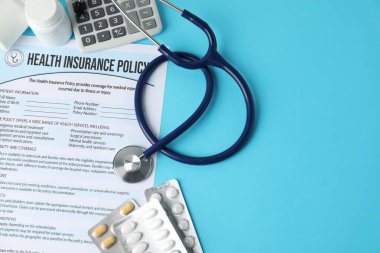 Sağlık sigortası poliçesi, steteskop, haplar ve hesap makinesi açık mavi arka plan, düz yatak. Metin için boşluk