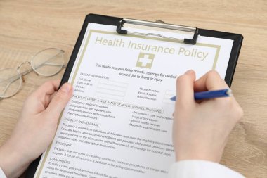 Tahta masada sağlık sigortası poliçesi dolduran doktor, yakın plan.