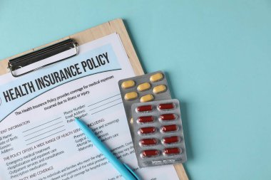 Sağlık sigortası poliçesi, turkuaz arka planda kalem ve haplar, üst tabaka. Metin için boşluk