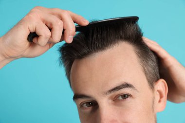 Yakışıklı adam saçını açık mavi arka planda taramış, yakın plan.