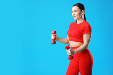 Spor kıyafetli kadın, açık mavi arka planda dambıllarla egzersiz yapıyor, metin için yer var.