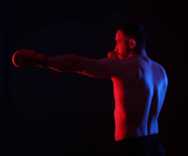 Boks eldivenli bir adam neon ışıklarda siyah arka planda dövüşüyor.