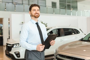 Kuaförde yeni arabaların yanında panosu olan mutlu bir satıcı.