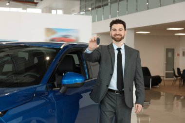 Yeni mavi arabanın yanında anahtarı olan mutlu bir satıcı.