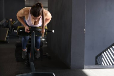 Spor salonundaki T-Bar sıra makinesinde ağırlık plakalı atletik kadın antrenmanı. Metin için boşluk