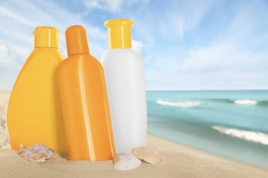 Okyanus yakınlarındaki kumlu sahilde güneş kremi ürünleri ve deniz kabukları.