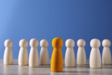 Farklılık, eşsizlik, bireysellik. Mavi arka plandaki ahşap figürler arasında turuncu insan figürü