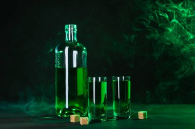 Absinthe shot bardakları, şişe ve esmer şeker siyah arka planda dumanlı