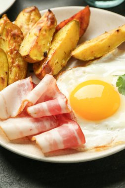 Lezzetli bir kahvaltı. Yağda yumurta, patates ve pastırma karanlık masada, yakın plan.