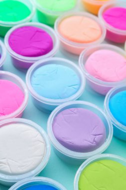 Açık mavi arka planda plastik kavanozlardaki farklı renkli modelleme killeri, yakın plan