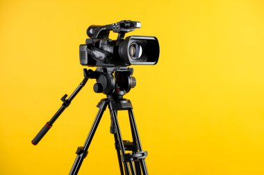 Sarı arkaplanda tripodu olan modern video kamera, metin için boşluk