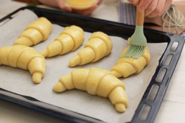 Beyaz masadaki çiğ kruvasanlara yumurta yıkayan kadın, yakın plan.