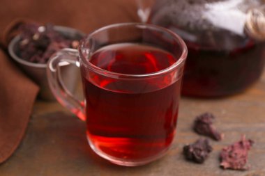 Cam fincanda leziz amber çayı, çaydanlık ve ahşap masada kuru gül sepalleri, yakın plan.