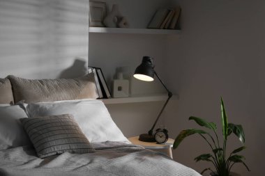 İçerideki komodinin üzerinde parlayan gece lambası ve çalar saat.