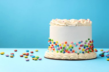 Açık mavi masaya renkli şekerlemeler serpiştirilmiş nefis bento keki, metin için yer.