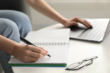 Beyaz masa içerisindeki çevrimiçi derste not alan bir kadın, yakın plan. Kendi kendine çalışma.