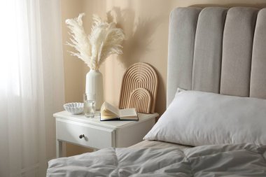 Yatağın yanında kitap, dekor ve bir bardak su olan komodin.