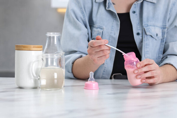 Mother making baby formula in feeding bottle at table indoors, closeup