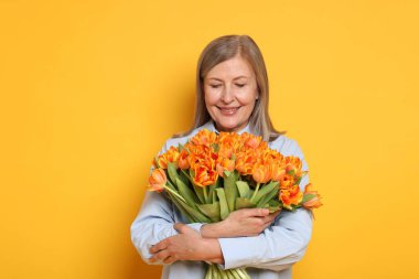 Sarı arka planda bir buket lale ile gülümseyen kadın.
