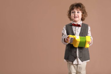 Kahverengi arka planda oyuncak akordeon çalan sevimli küçük çocuk.