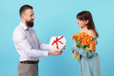 Bir buket güzel lalesi olan kadın açık mavi arka plandaki adamdan hediye paketi alıyor.