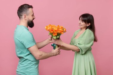 Adam pembe arka planda sevgili karısına bir buket güzel lale sunuyor.