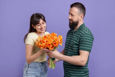 Adam mor arka planda sevgili karısına kırmızı güller sunuyor.