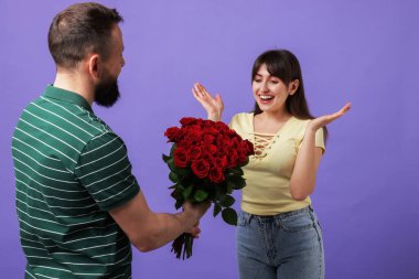 Adam mor arka planda sevgili karısına kırmızı güller sunuyor.