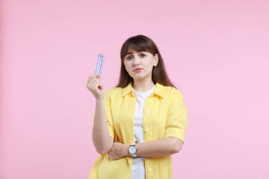Pembe arka planda doğum kontrol hapları taşıyan üzgün bir kadın.
