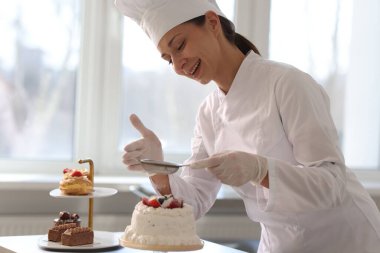 Şekerci, mutfaktaki kekin üzerine pudra şekeri serpiyor.